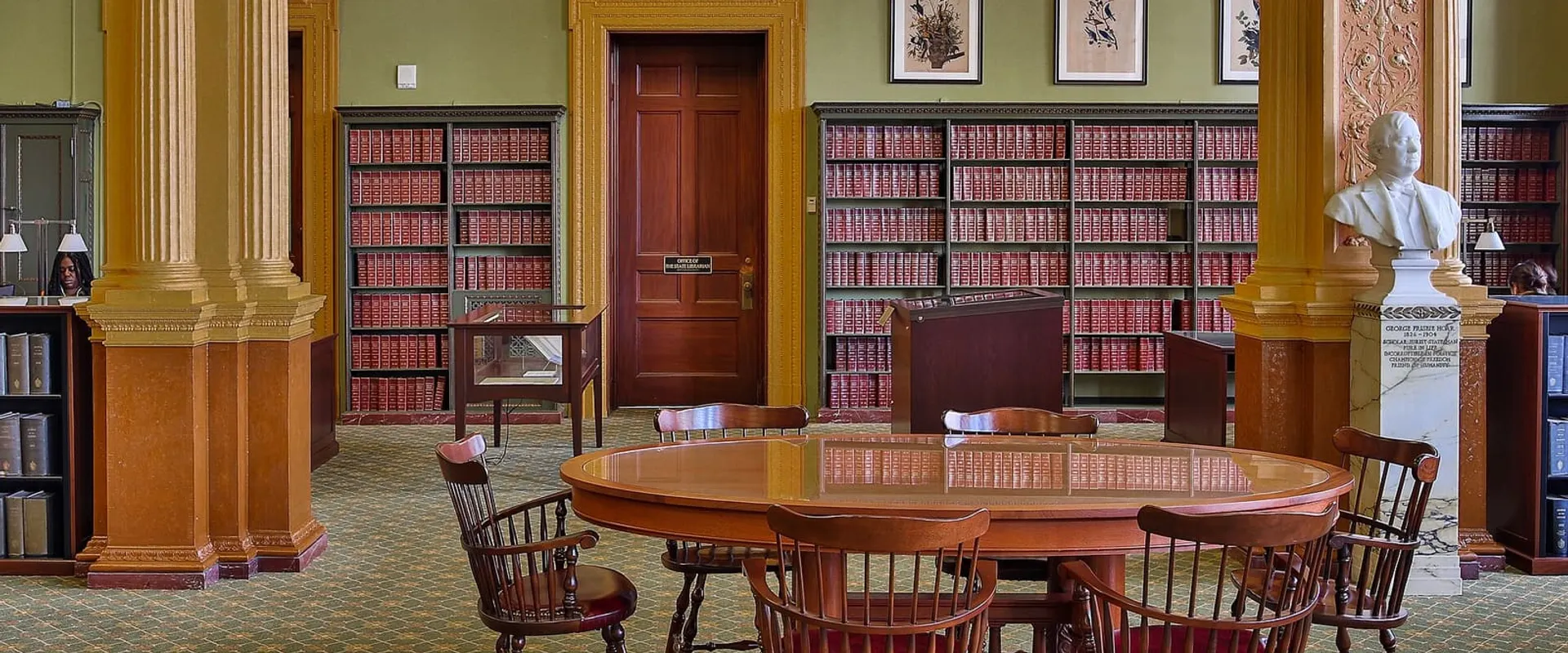 Sala della biblioteca con un grande tavolo rotondo, sedie in legno e scaffali di libri