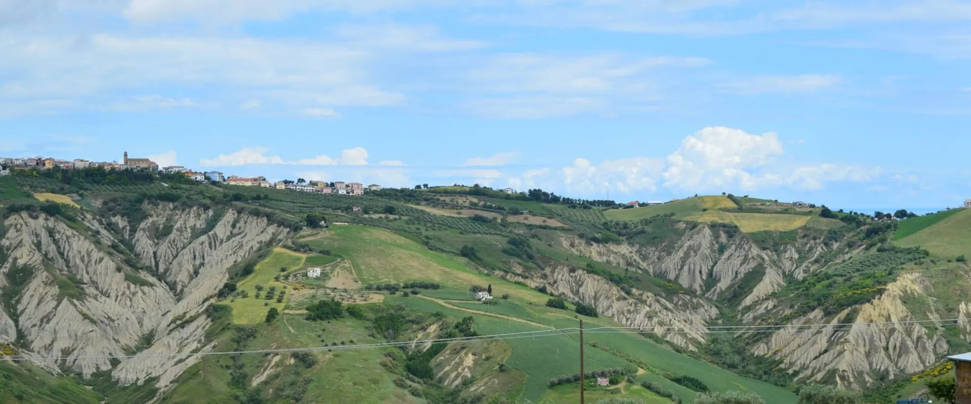 Colline con i calanchi d’argilla e i campi verdi, con un paese sul crinale in lontananza