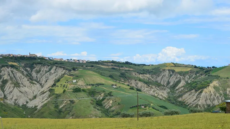 Colline con i calanchi d’argilla e i campi verdi, con un paese sul crinale in lontananza