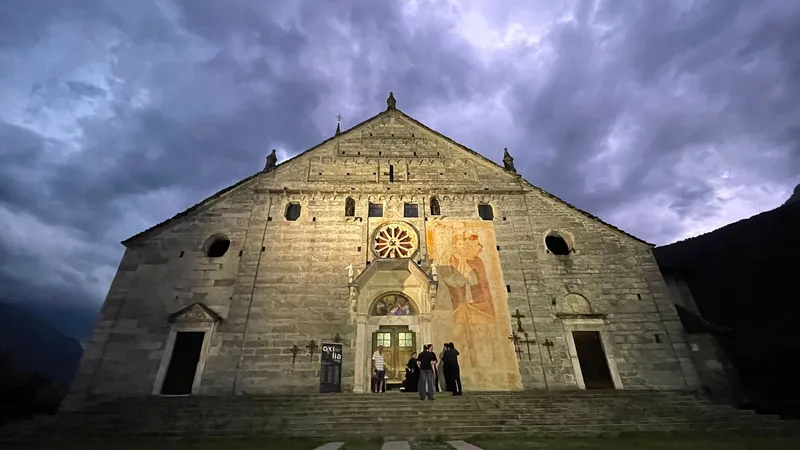 Facciata in pietra della chiesa con il rosone e un grande affresco, al tramonto