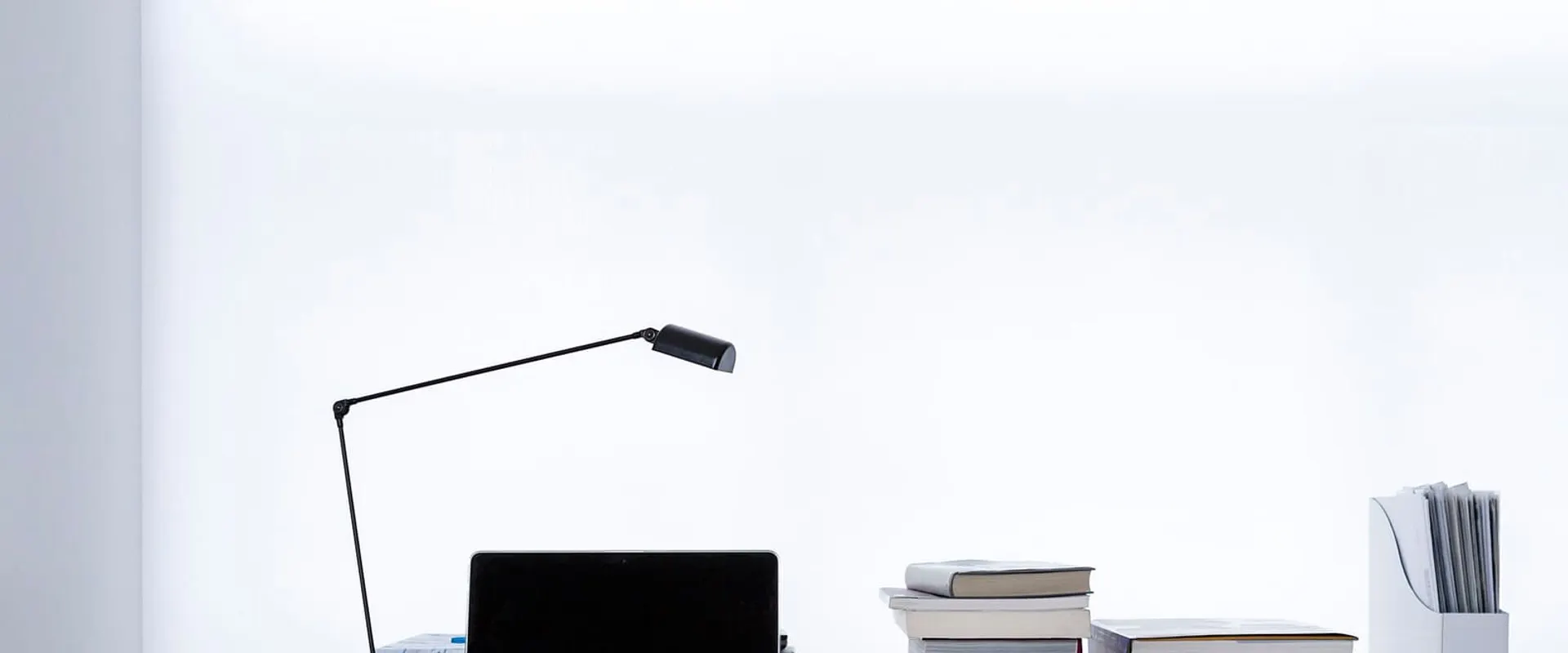 Computer portatile aperto su una scrivania bianca accanto a una pila di libri