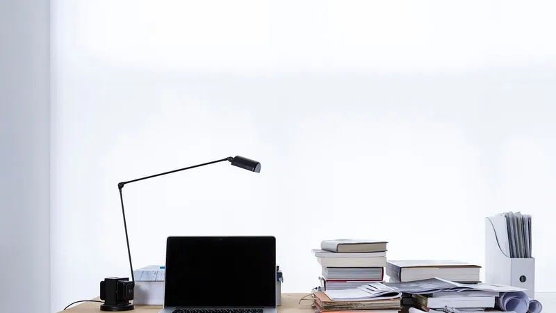 Computer portatile aperto su una scrivania bianca accanto a una pila di libri