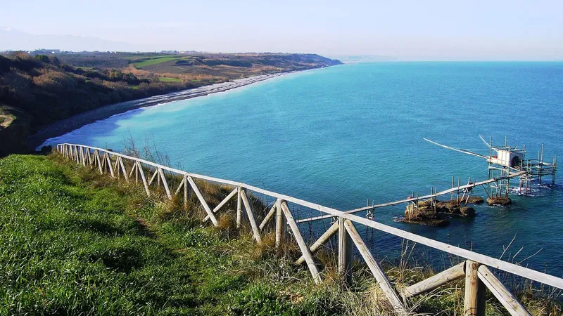 Vista dall’alto della costa con il mare azzurro, la staccionata del belvedere e un trabocco in basso