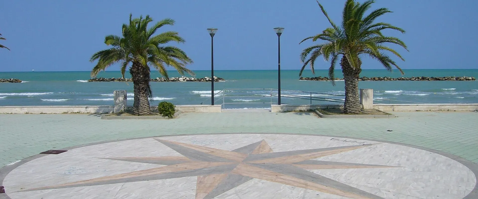 Piazzetta sul lungomare con la rosa dei venti disegnata sul pavimento e due palme