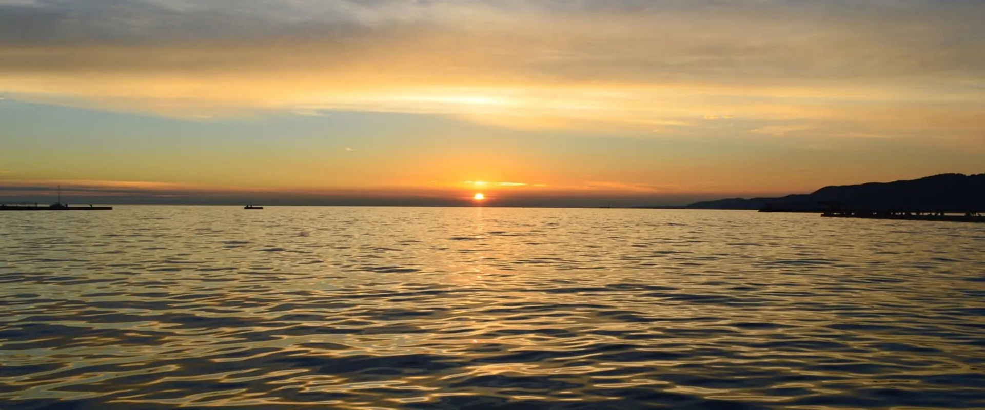 Il sole che tramonta sul mare calmo, con le nuvole basse all’orizzonte