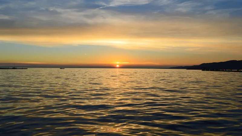 Il sole che tramonta sul mare calmo, con le nuvole basse all’orizzonte