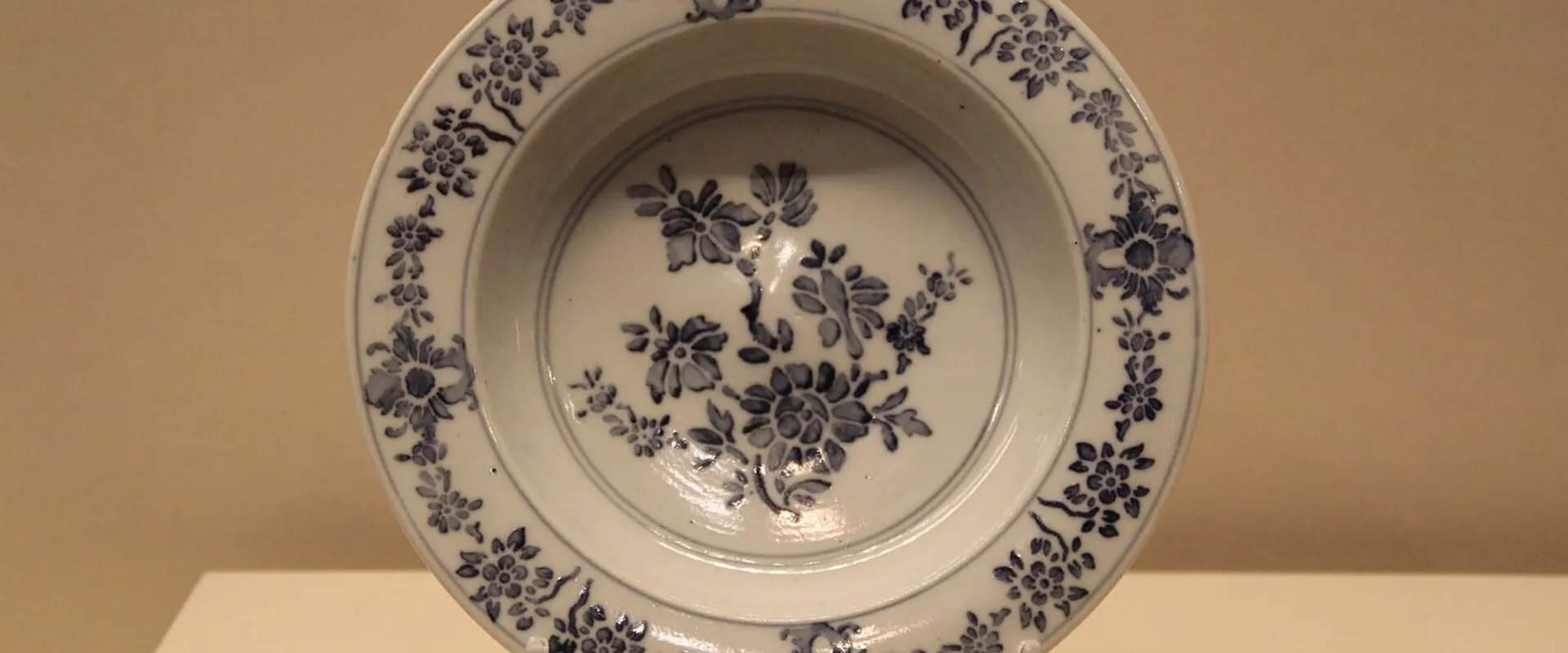 Piatto in ceramica bianca decorato con fiori blu, esposto in una vetrina