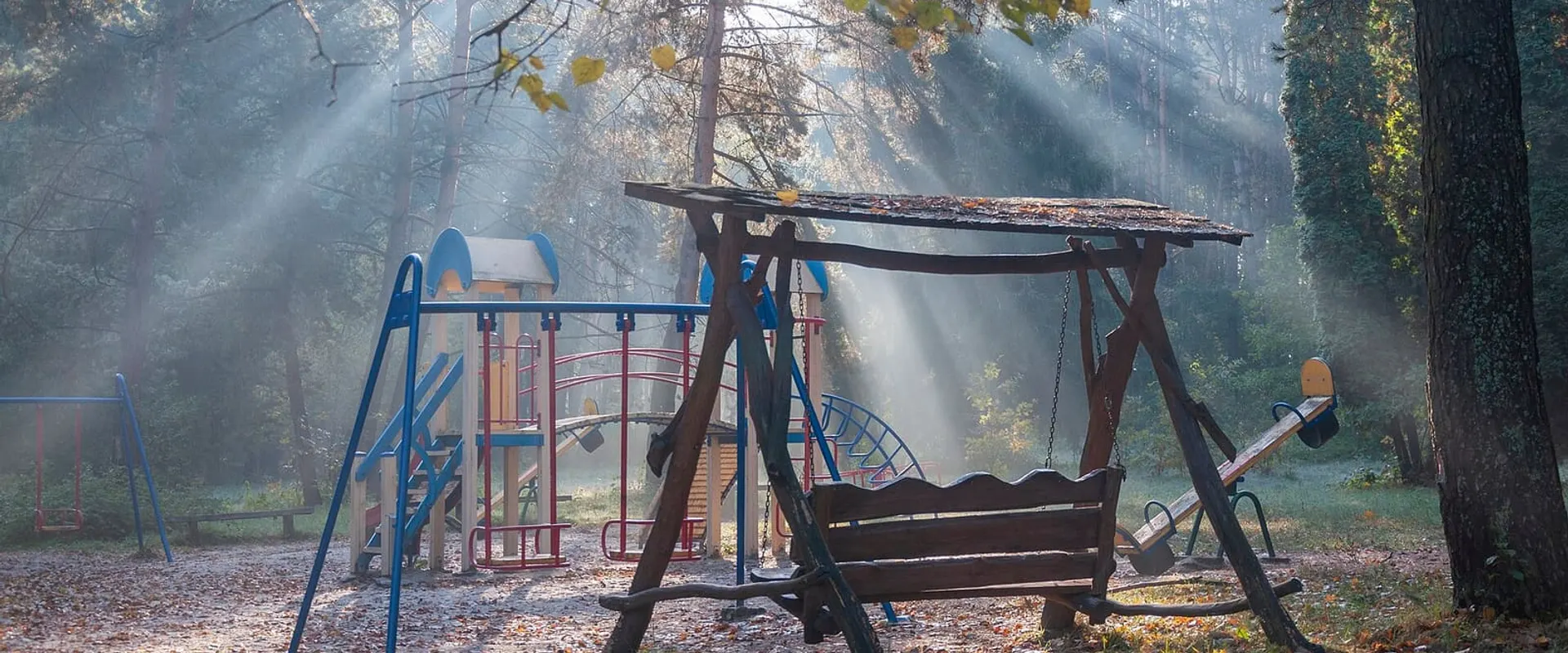 Area giochi del parco con altalene e scivoli tra gli alberi, illuminata dal sole del mattino
