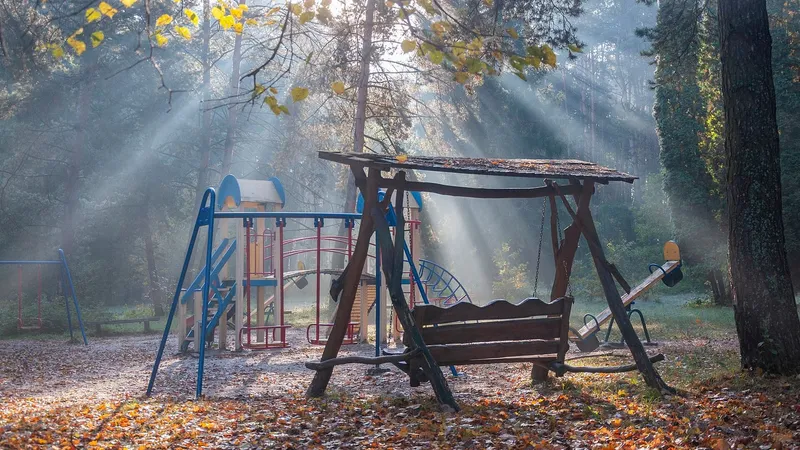 Area giochi del parco con altalene e scivoli tra gli alberi, illuminata dal sole del mattino