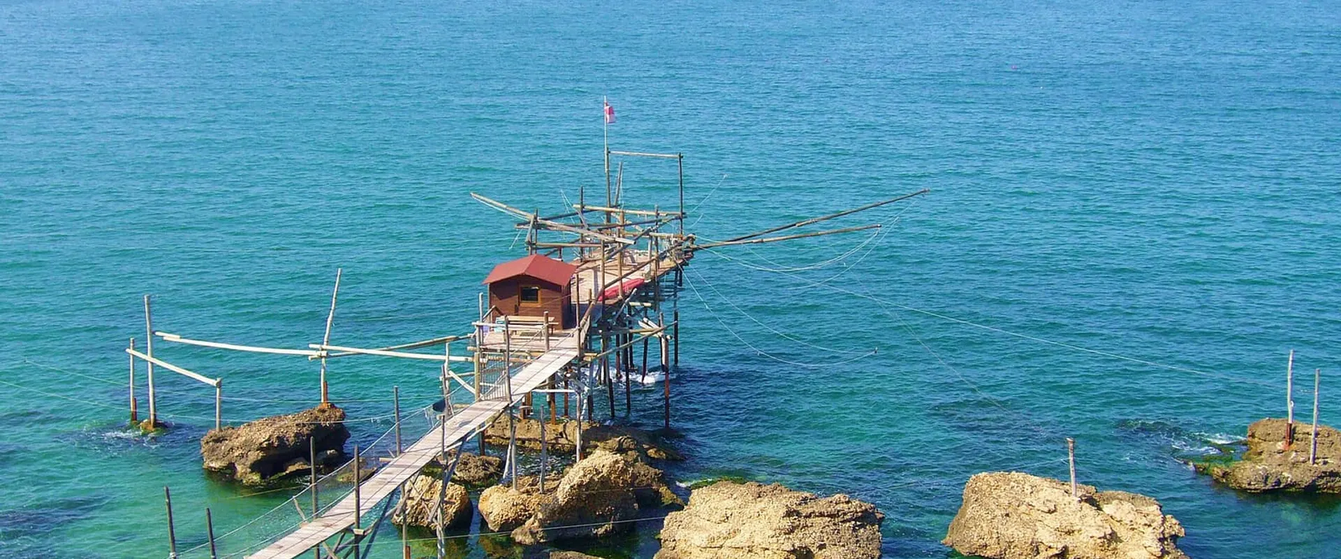 Trabocco in legno su palafitte sopra il mare turchese, collegato agli scogli da una passerella